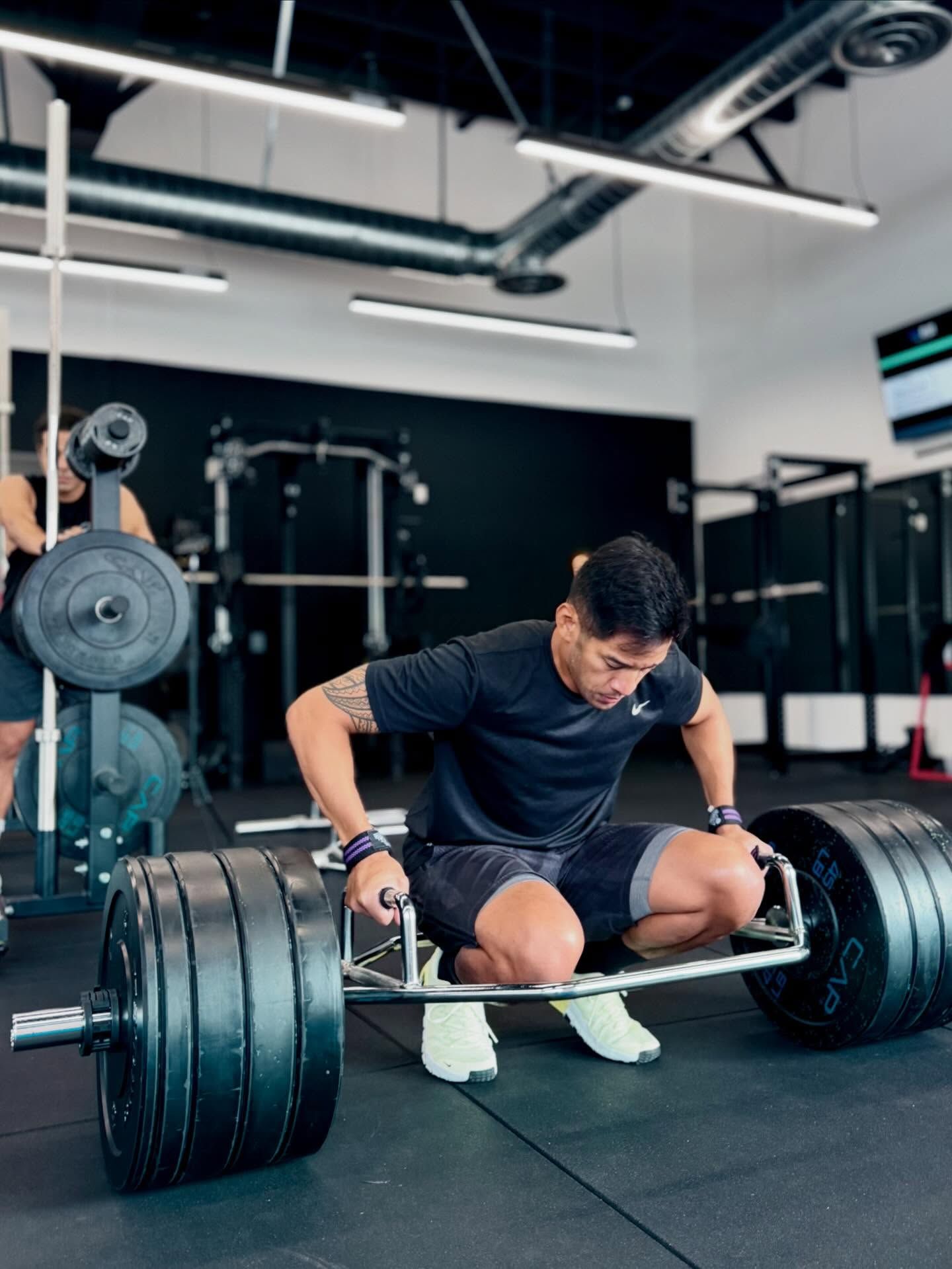 Man performing a deadlift in a gym, holding a hex bar loaded with weights.