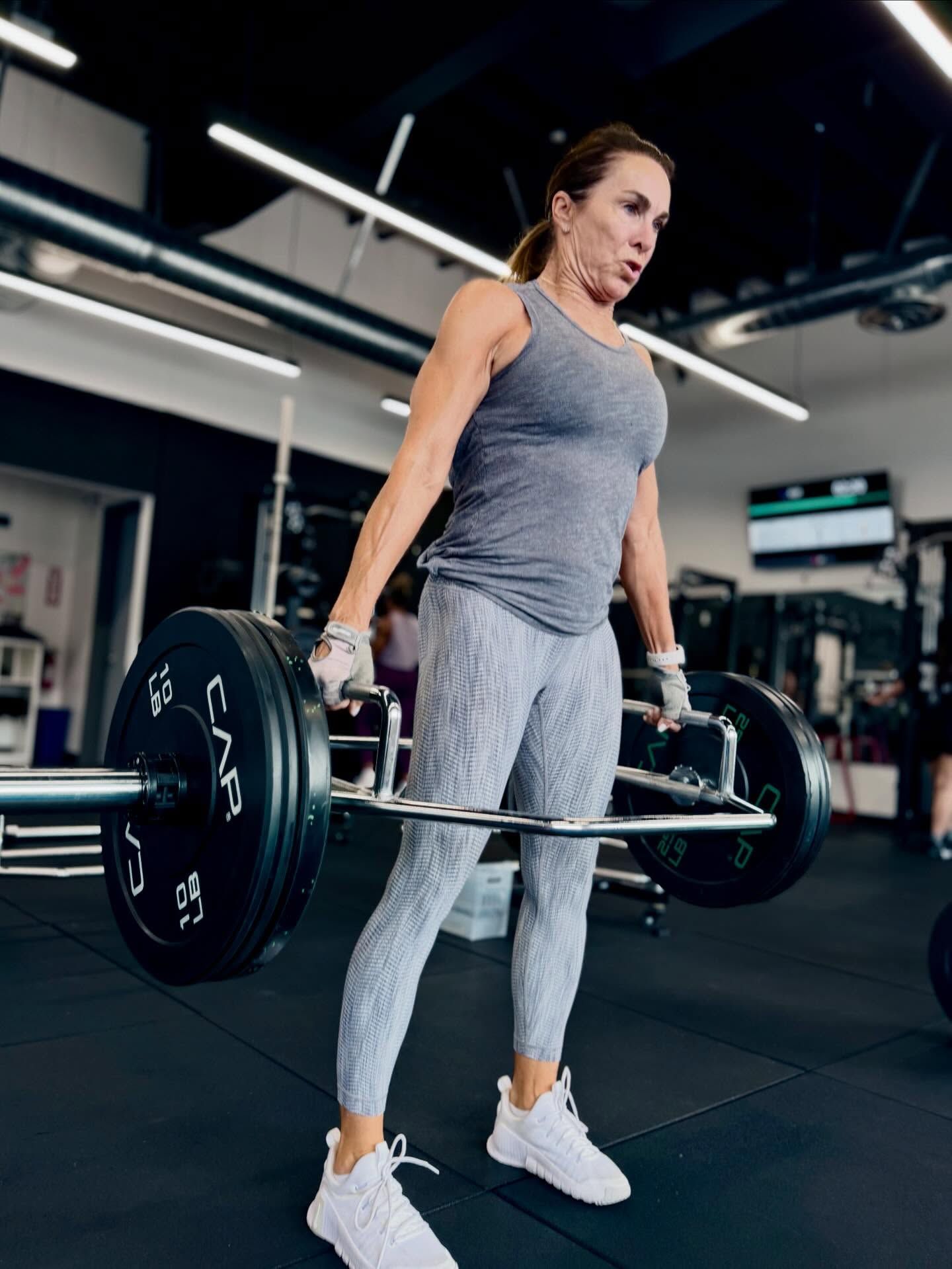 Woman lifting a barbell in a gym, wearing workout clothes.