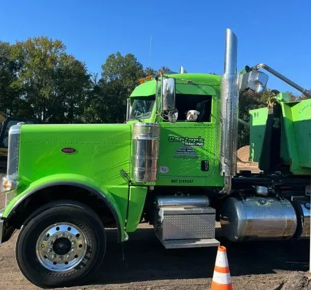 Green Peterbilt truck with a large chrome exhaust pipe, parked on a sunny day.