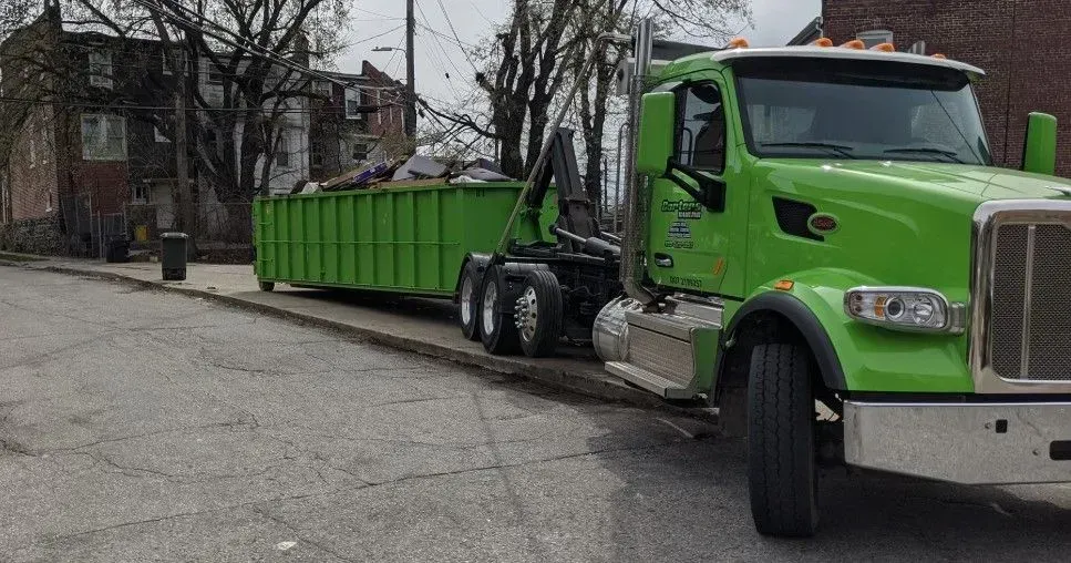 Green dump truck with a green container parked on a street in front of a building.