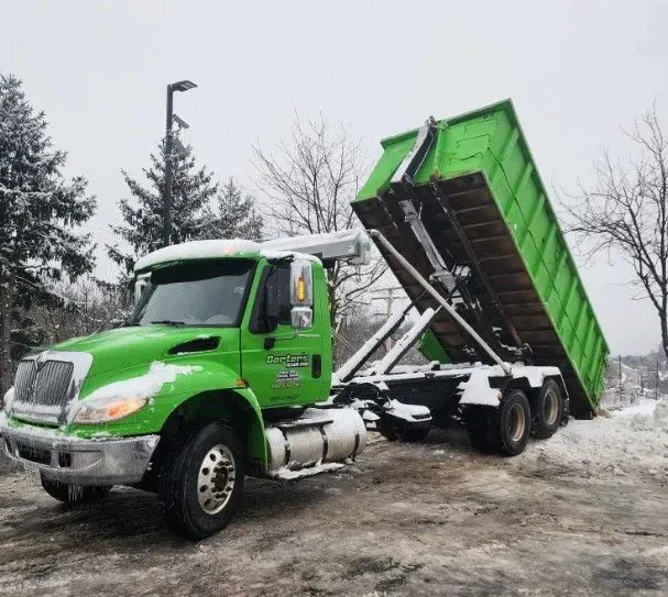 Green dump truck with a raised dumpster in a snowy setting.