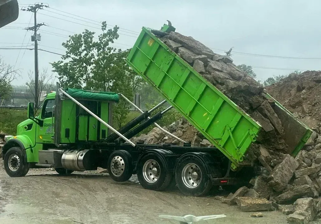 Green dump truck unloading rubble.
