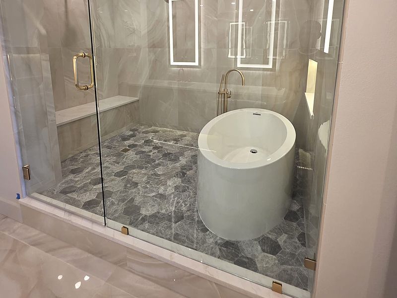 Modern bathroom with a round tub and shower enclosed by glass walls, gray and white tile.