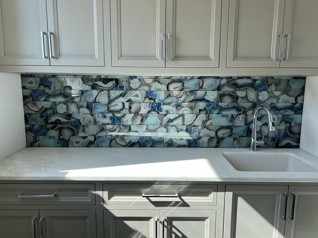 a kitchen with white cabinets , a sink , and a blue tile backsplash .