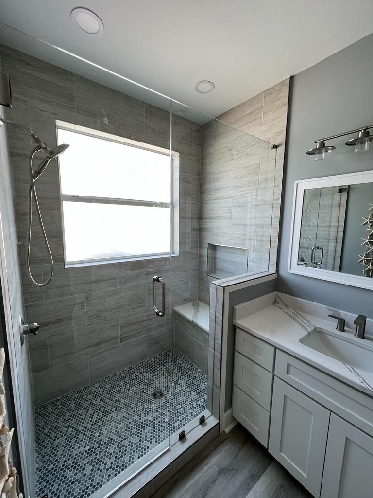 a bathroom with a walk-in shower, sink, mirror, and window