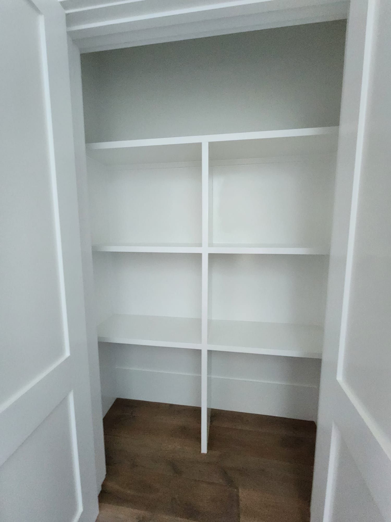 an empty closet with white shelves and a wooden floor
