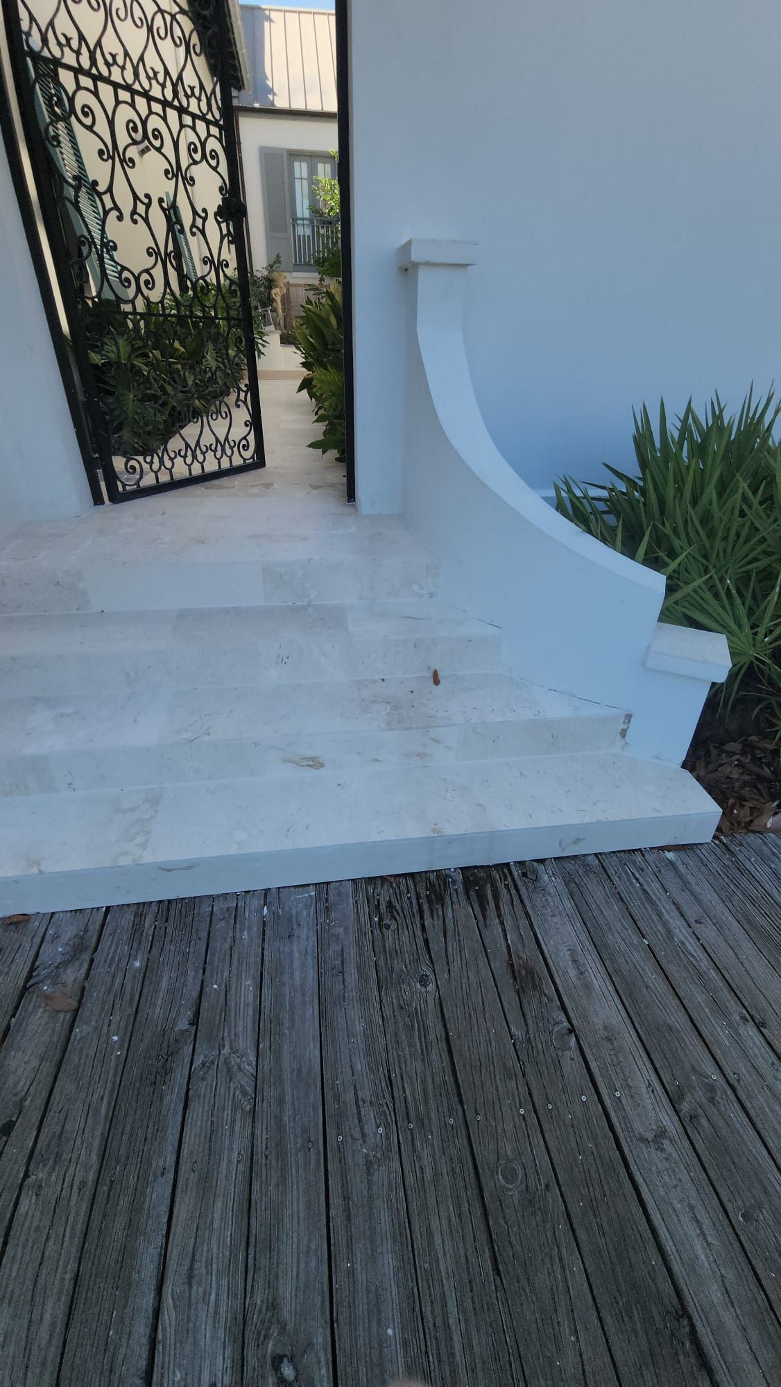 a wooden deck next to a white building with stairs and a gate