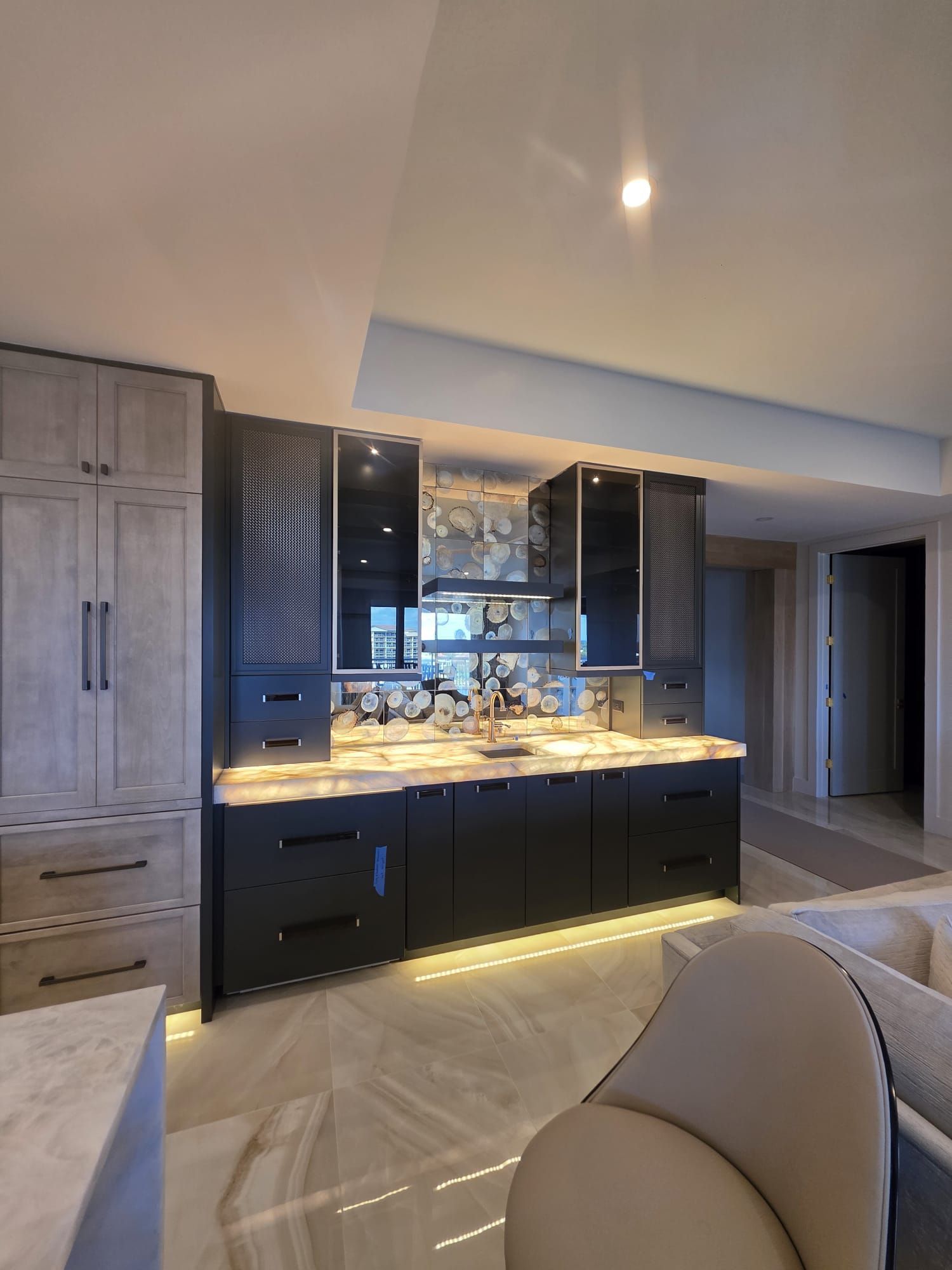 Stylish modern wet bar with black cabinets, marble countertop, and under-cabinet lighting.