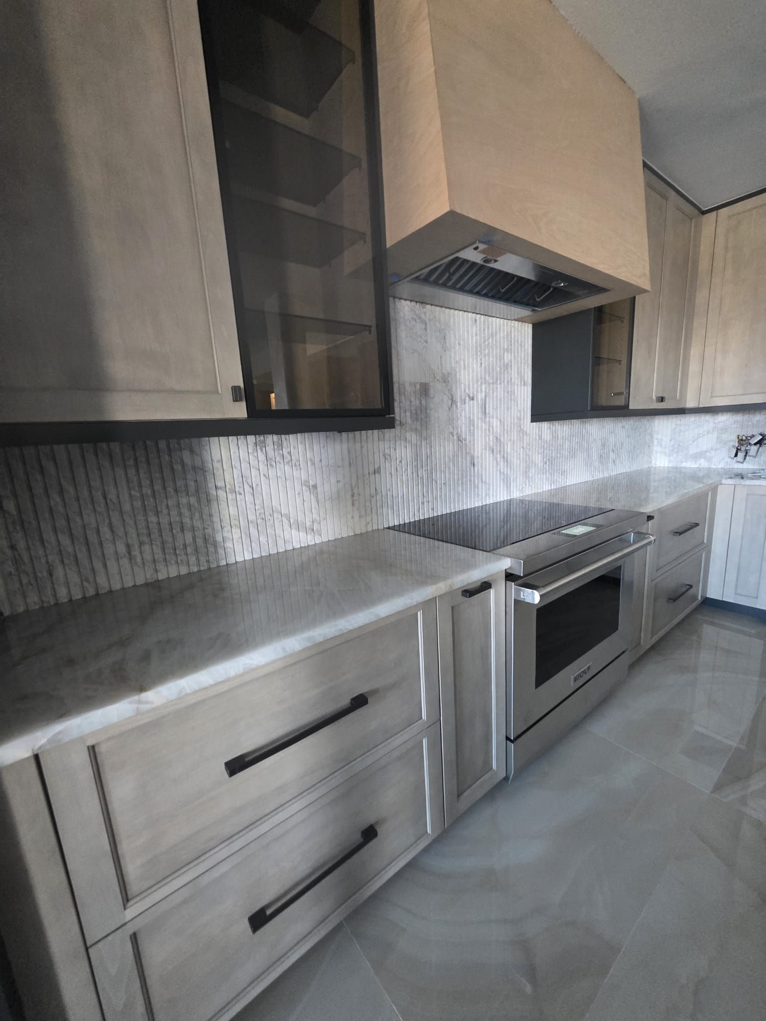 Modern kitchen with light wood cabinets, stainless steel appliances, and marble backsplash.