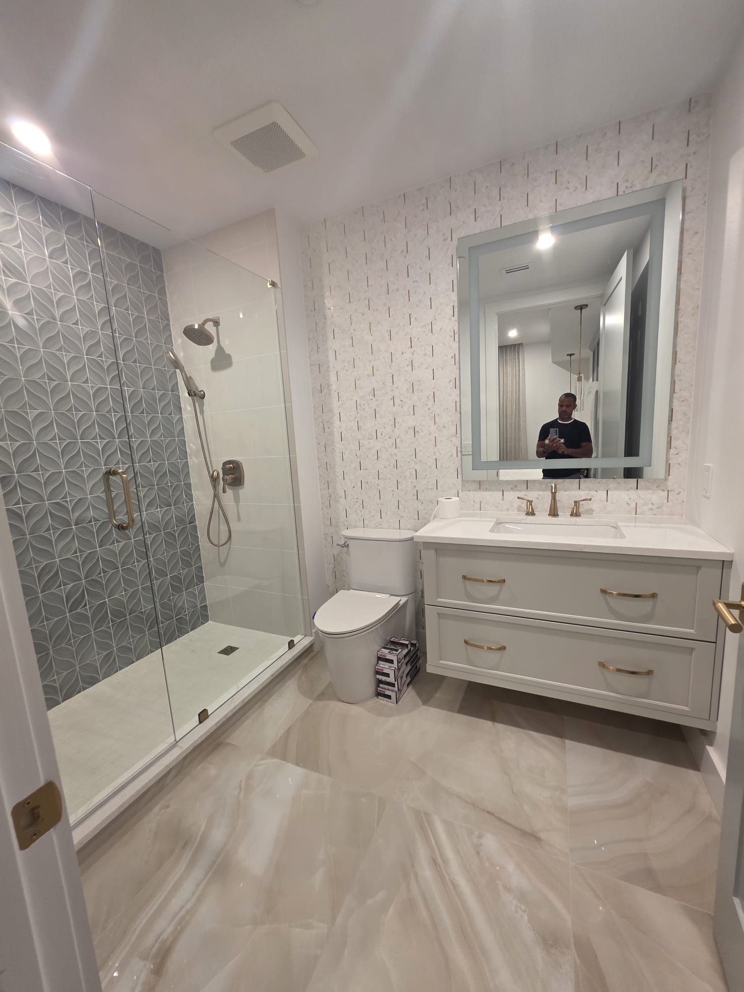 Modern bathroom with a glass shower, patterned tile accent wall, vanity, and large mirror.