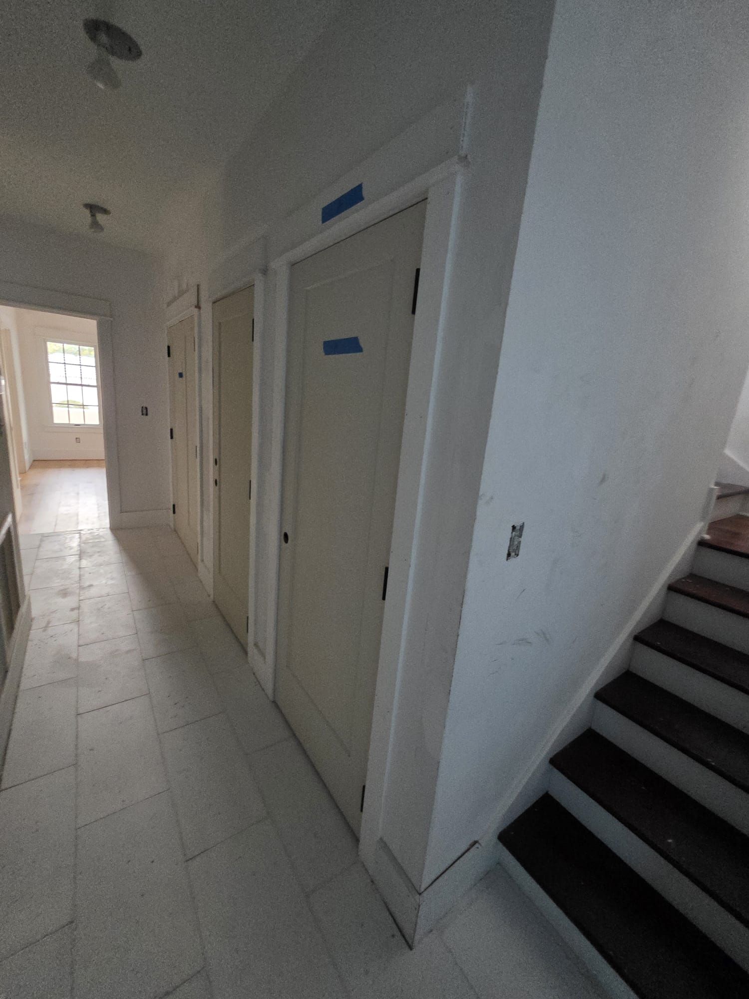 Hallway with doors, stairs to the right, tile floor, and a window at the end.