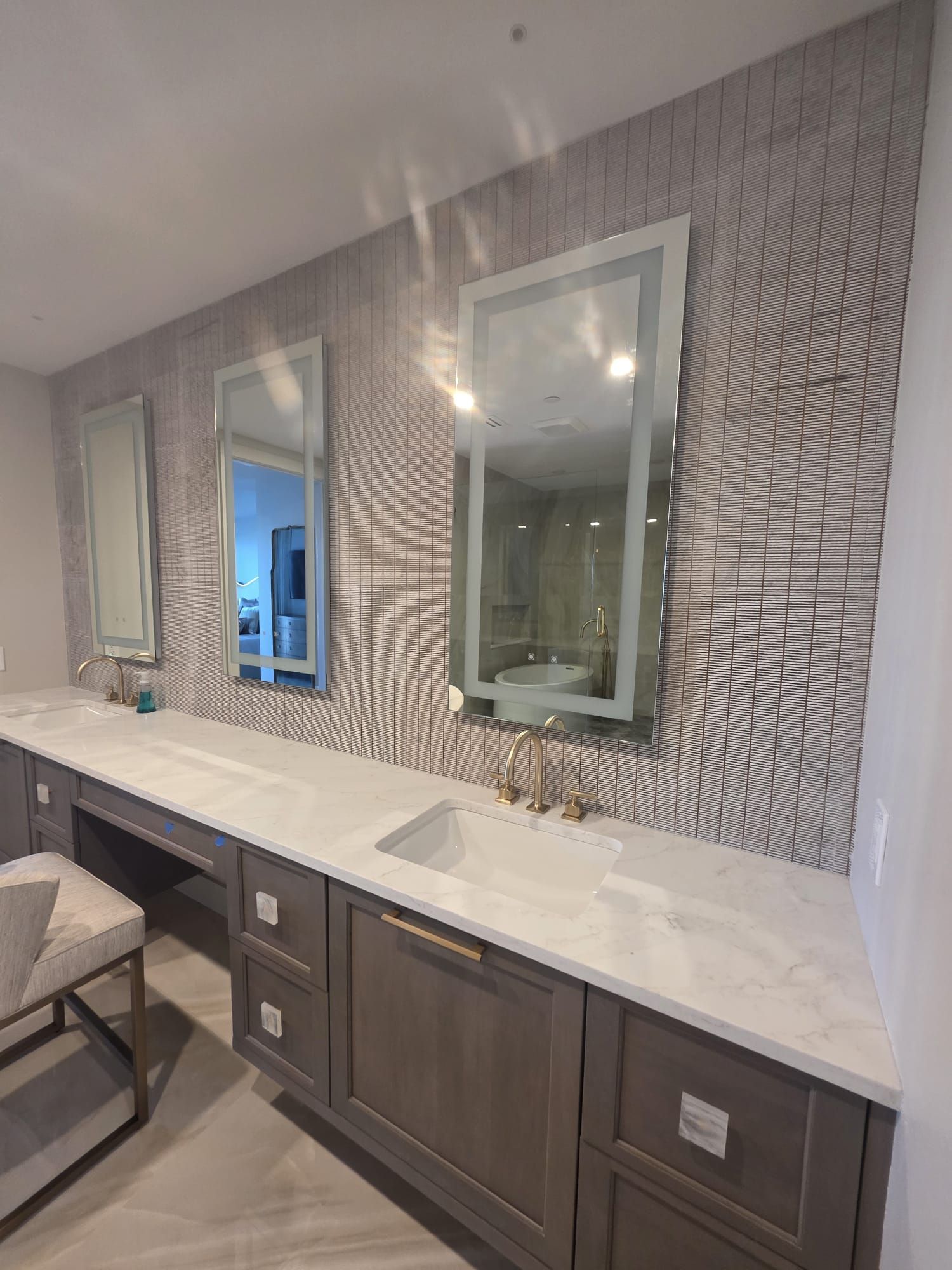 Bathroom vanity with gray cabinets, white countertop, three mirrors, and textured wall.