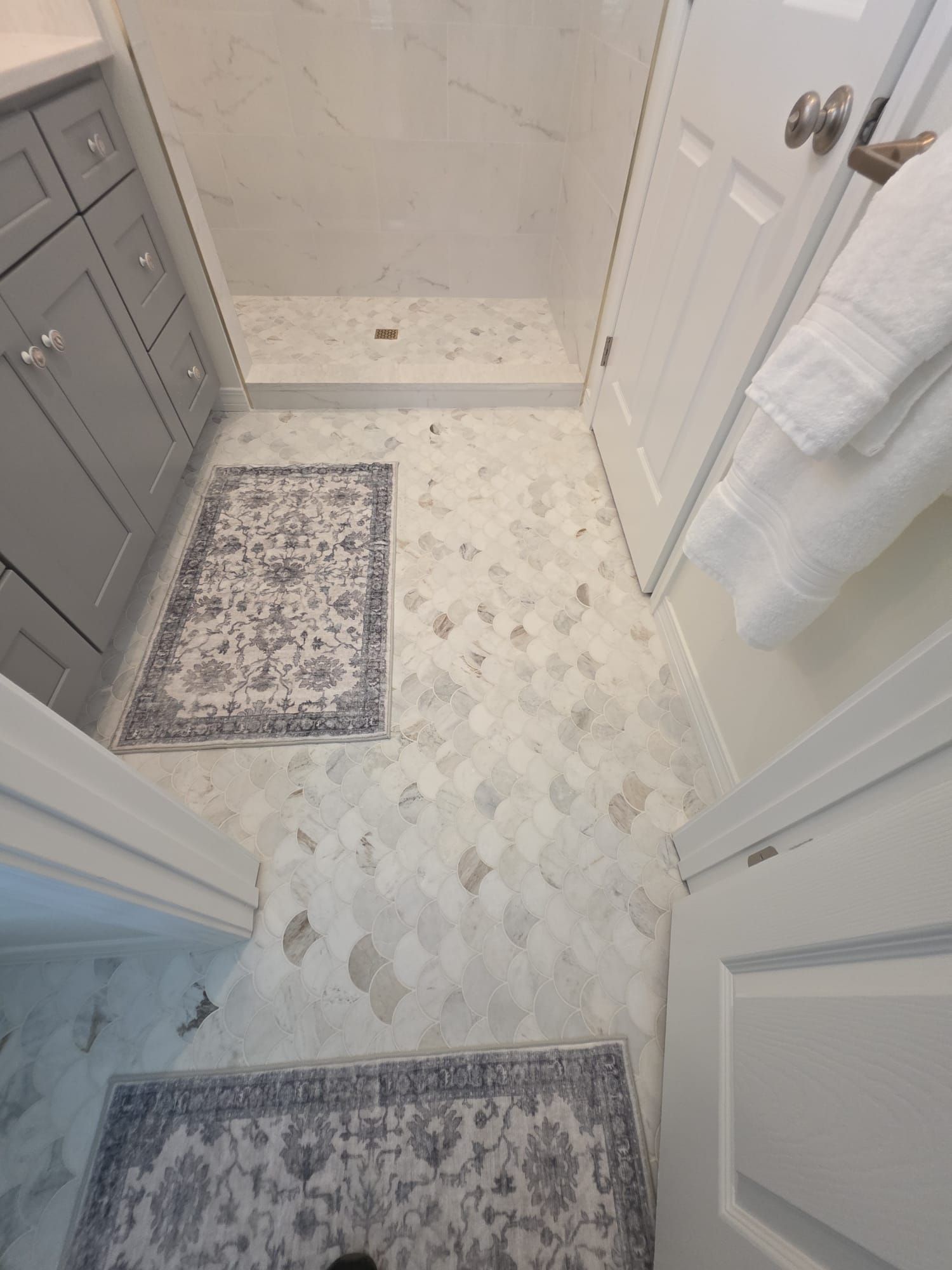Bathroom with gray cabinetry, white door, and patterned tile floor; two small rugs.