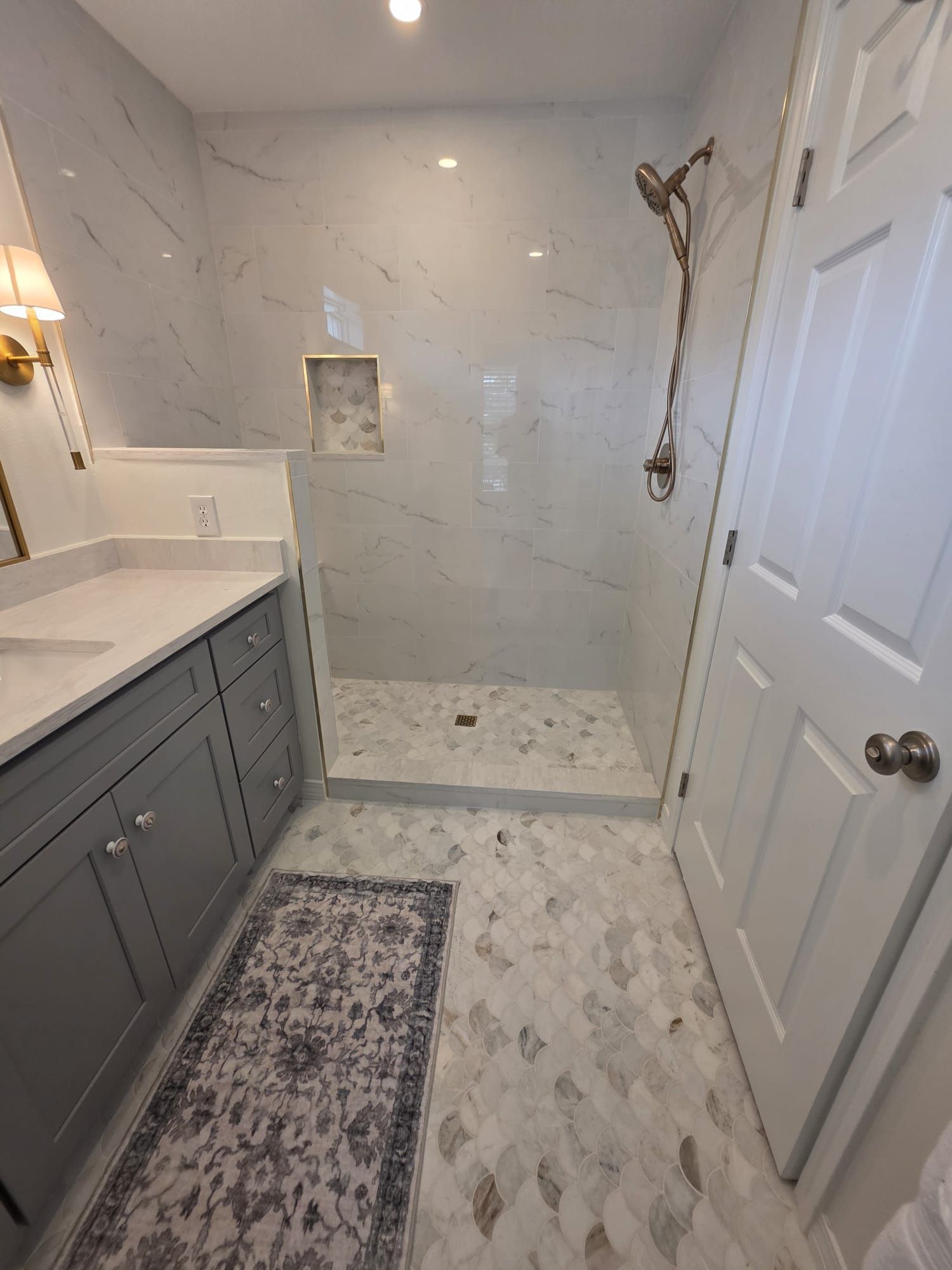 Bathroom with gray vanity, marble shower, and patterned floor tile.