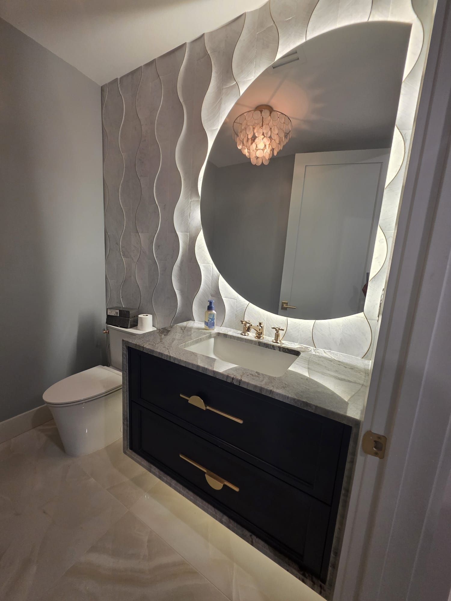 Modern bathroom with decorative wave-patterned wall, large illuminated mirror, floating vanity, and toilet.