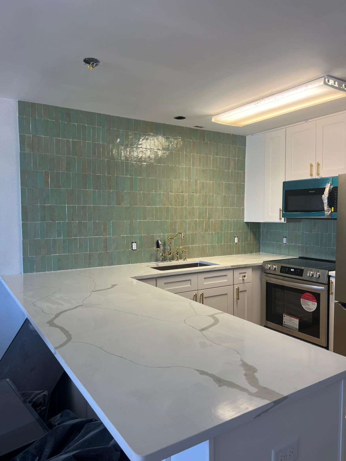 Newly remodeled kitchen with light green tile backsplash, white countertops, and white cabinets.