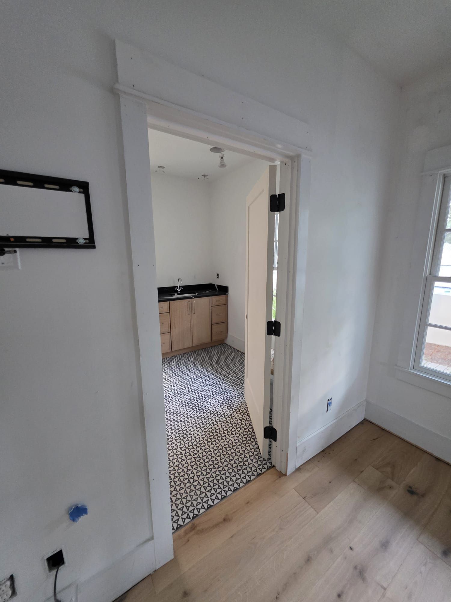 Open doorway into a room with black and white patterned tile flooring, wood cabinets, and a window.