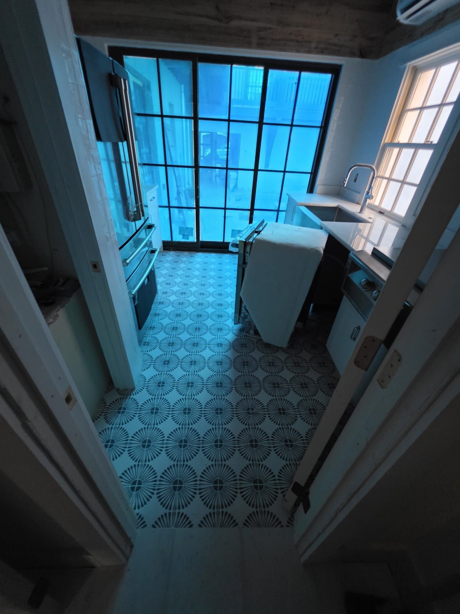 Narrow kitchen with patterned floor, large blue window, and appliances.