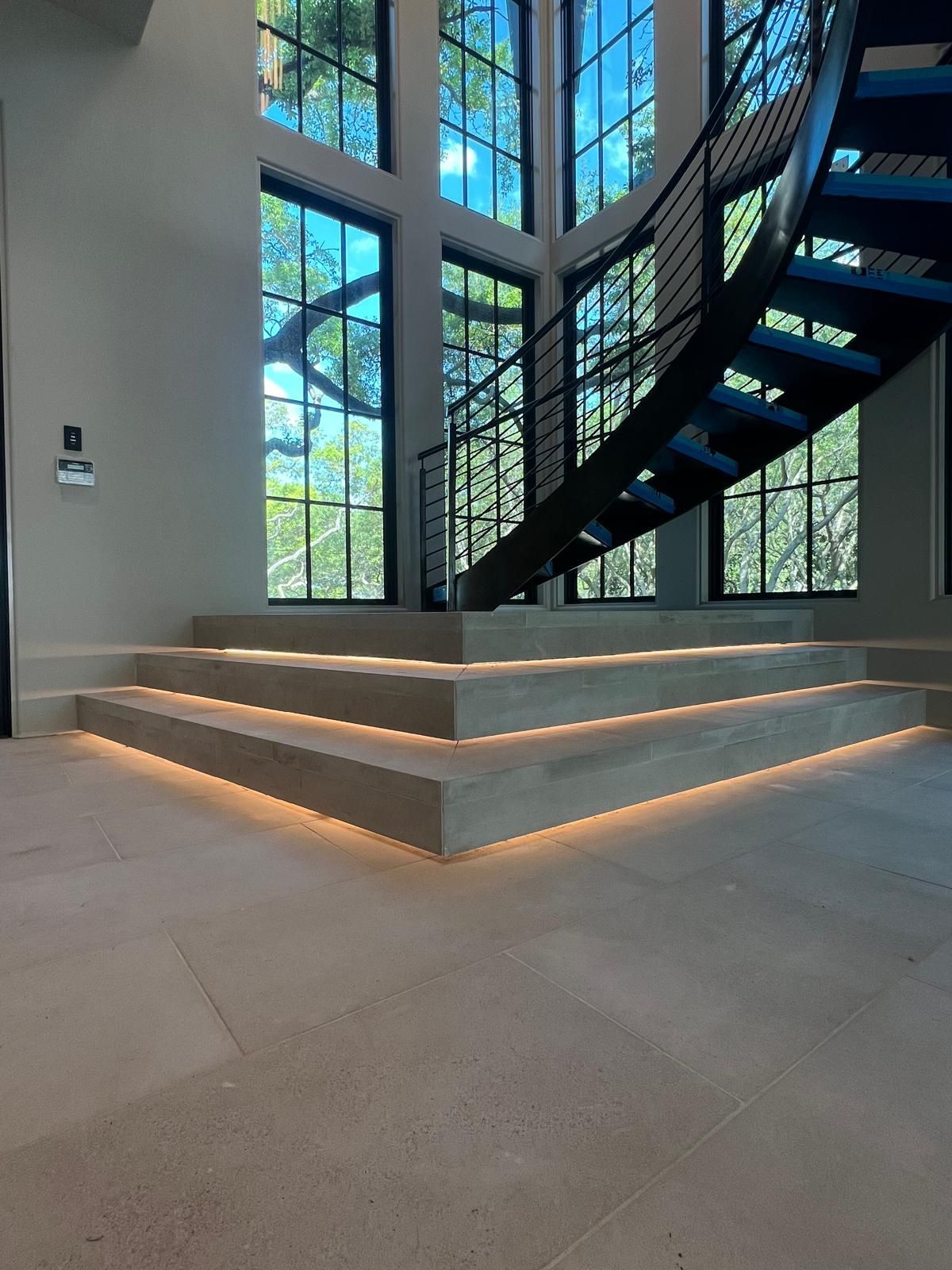 Modern staircase with integrated lighting, next to large windows.