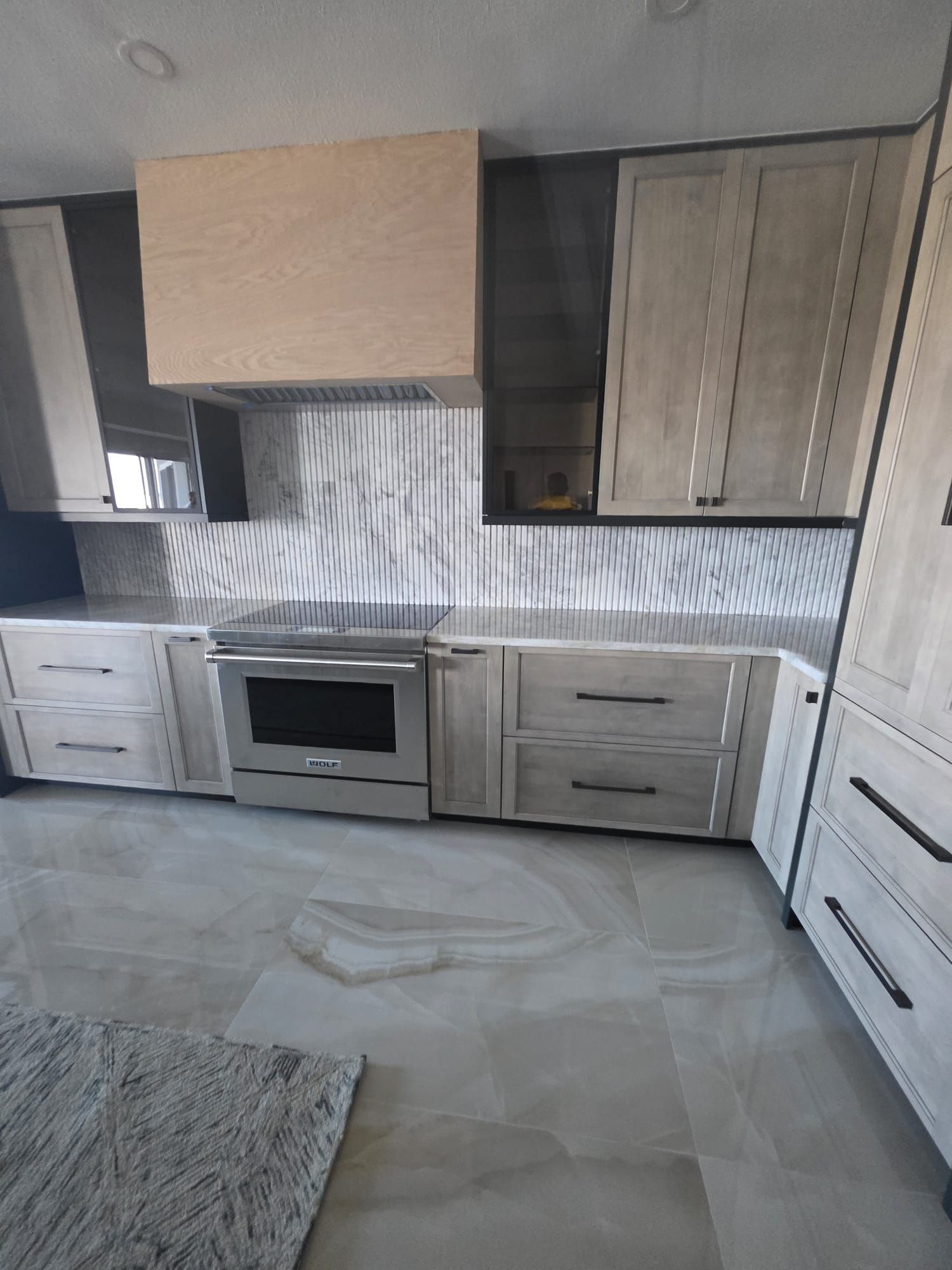 Modern kitchen with light wood cabinets, stainless steel appliances, and gray countertops.