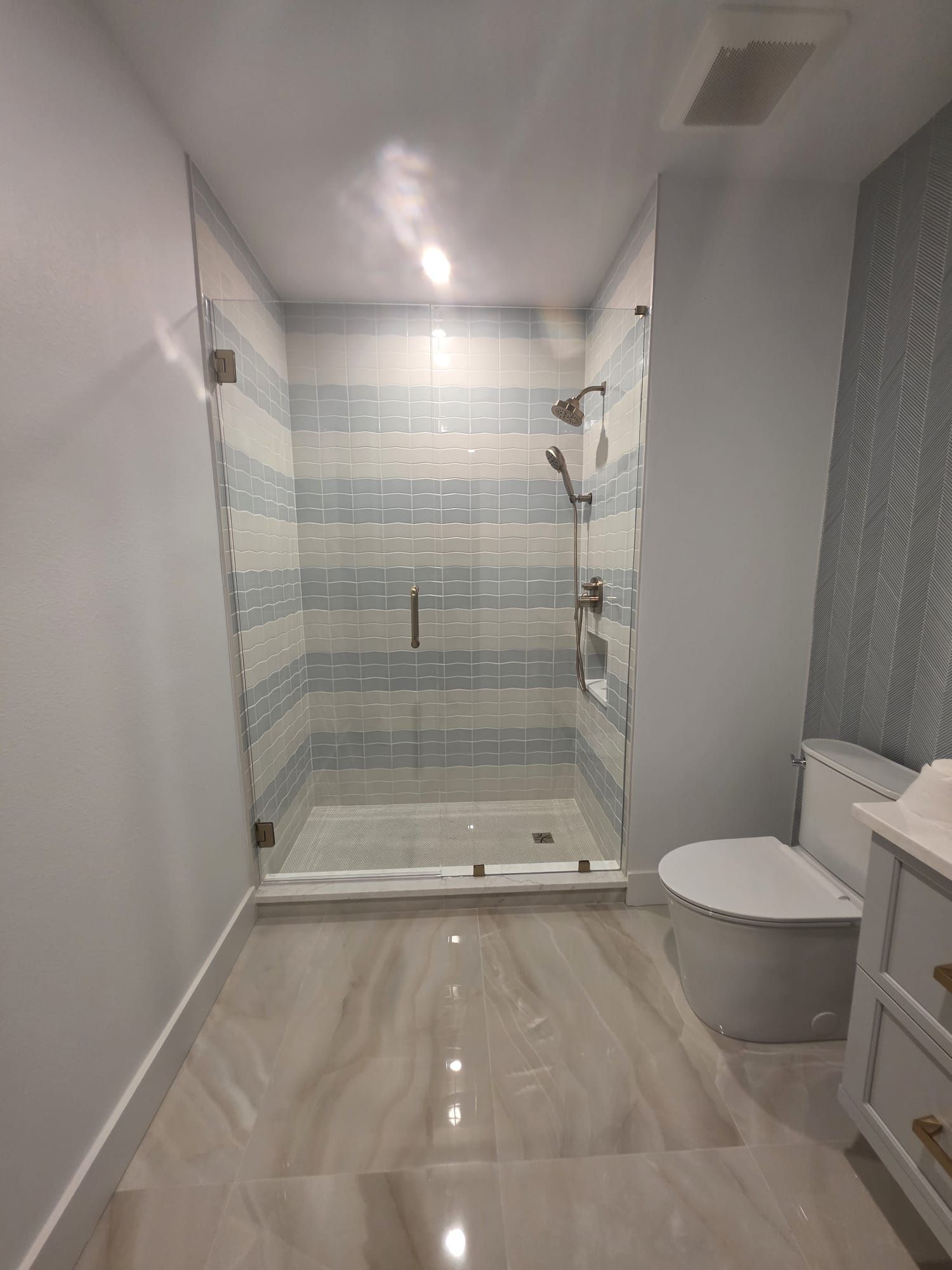 Bathroom with a glass-enclosed shower, blue and white tiled walls, and a white toilet.