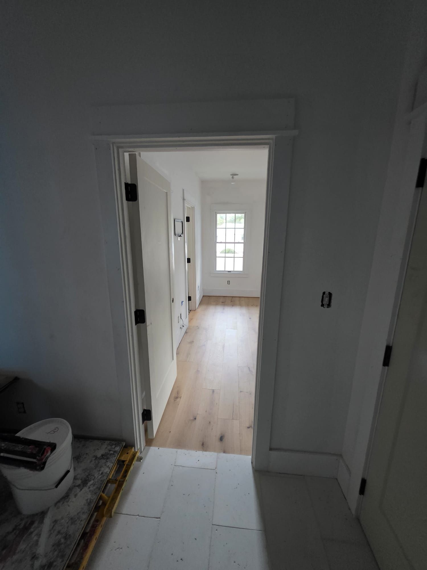 Hallway with white walls, doors, and trim; wood floors; natural light from a window at the end.