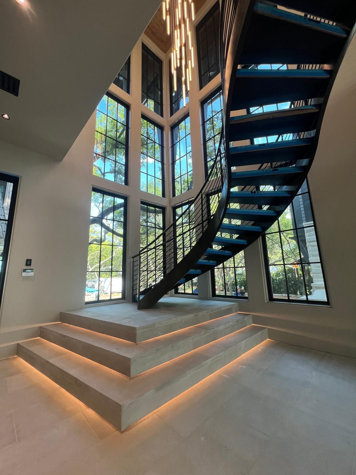 Elegant curved staircase with black metal railing, leading up to large windows. Lit steps.