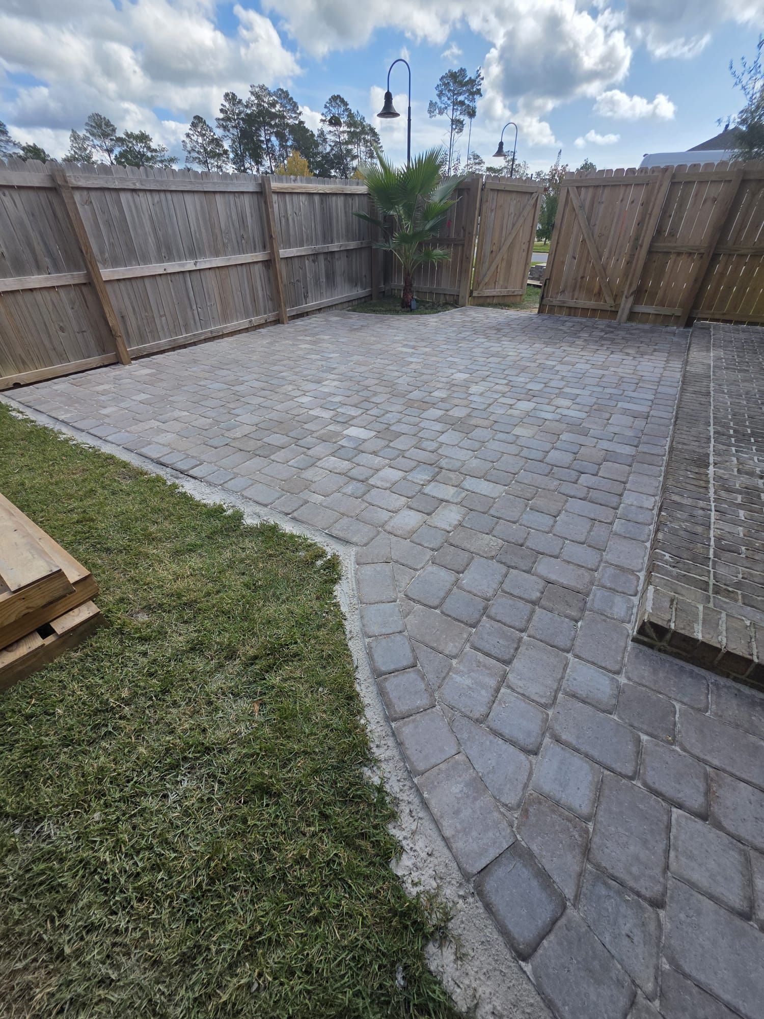 A paved patio surrounded by a wooden fence and grass lawn.