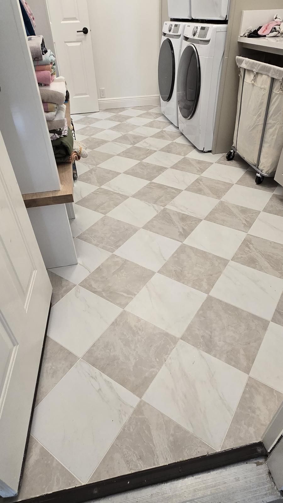 Laundry room with checkered floor tiles in shades of beige and white. Washing machine, dryer, and cabinet visible.