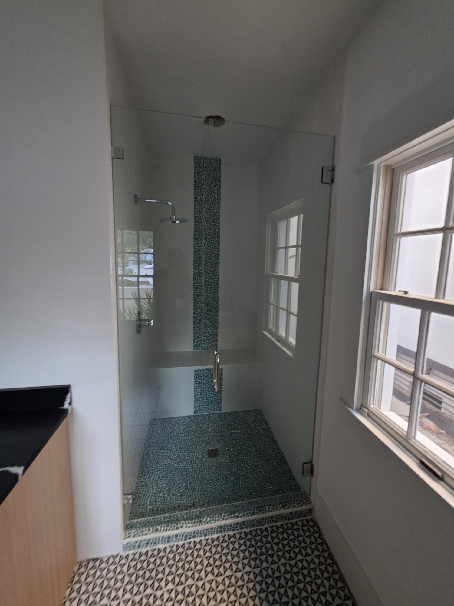 Shower with glass door, mosaic tile accent, and two windows in a white-walled bathroom.