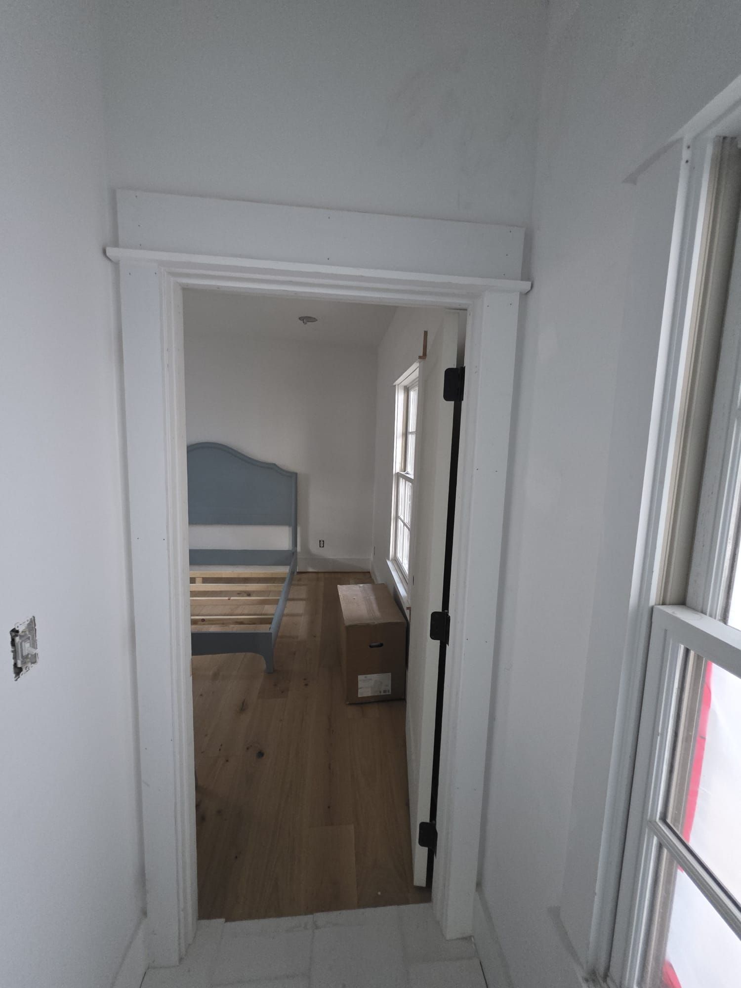 White doorway leading to a room with wood flooring, and a window.