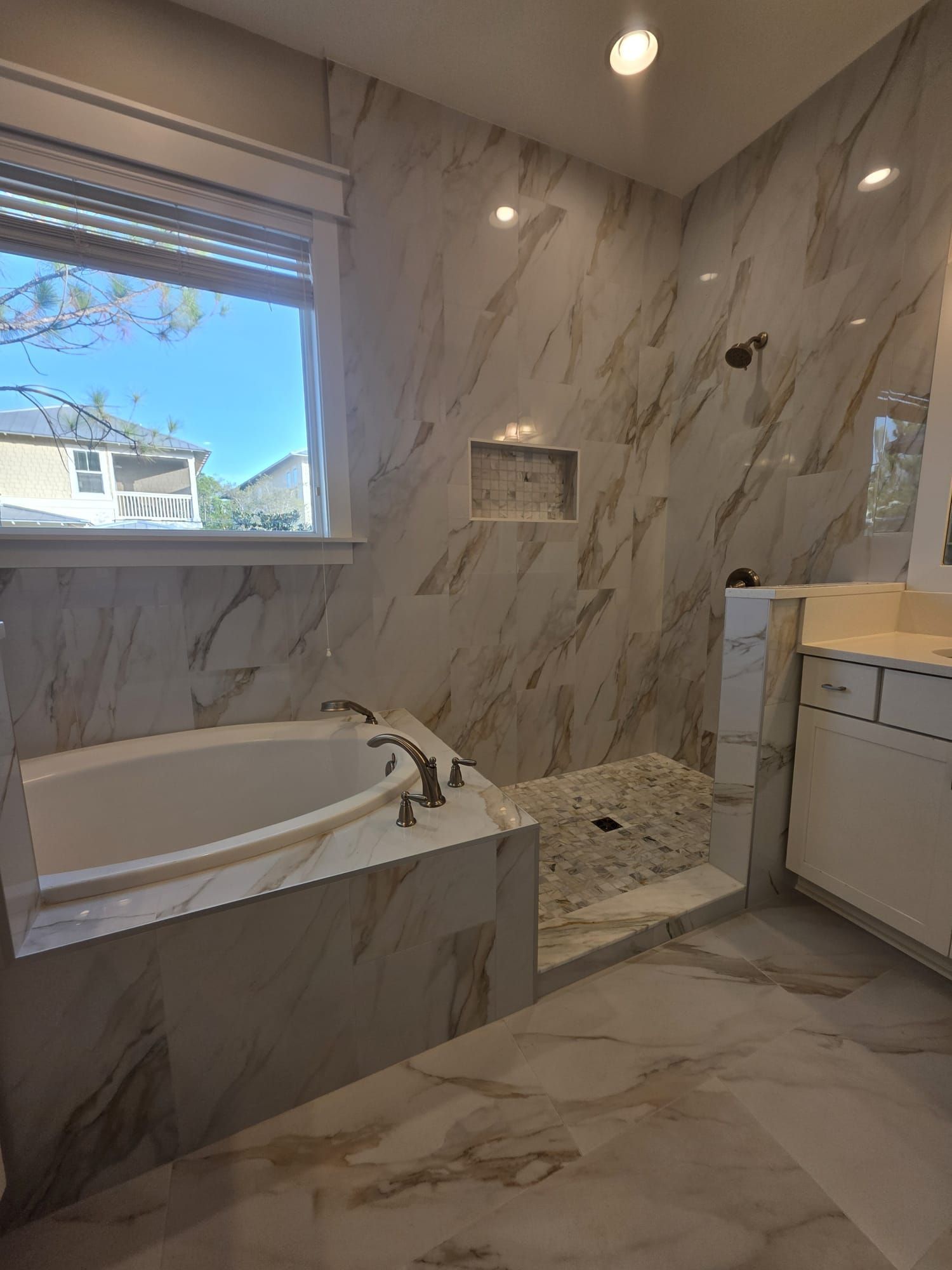 Bathroom with marble-look tile, a tub, shower, vanity, and window.