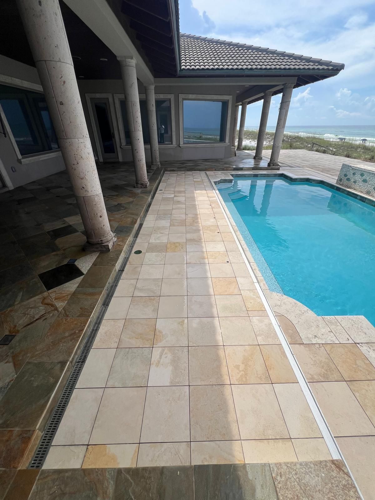 Patio with pool, beach view, tile flooring, stone columns, and covered porch.