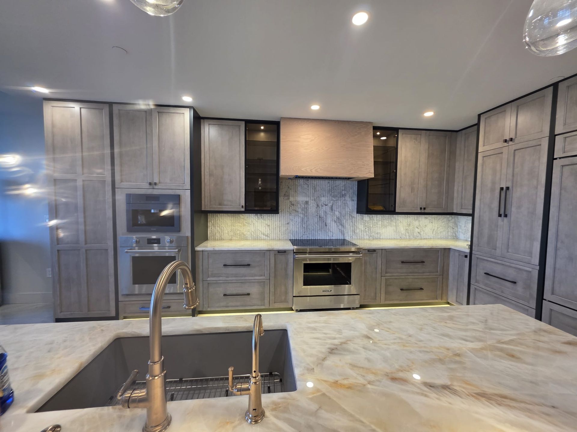 Modern kitchen with light gray cabinetry, stainless steel appliances, and a marble countertop island.