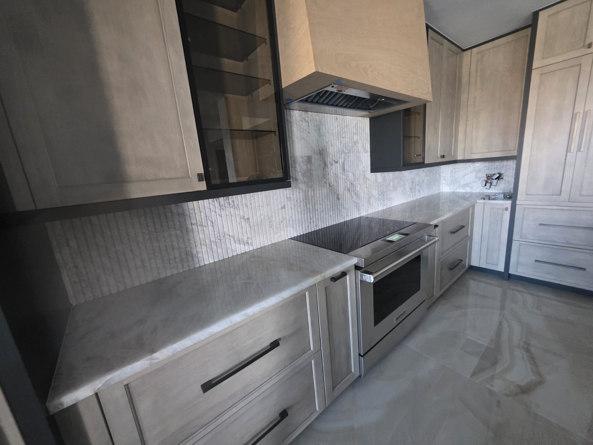 Modern kitchen with light wood cabinets, gray countertops, stainless steel appliances, and tile backsplash.