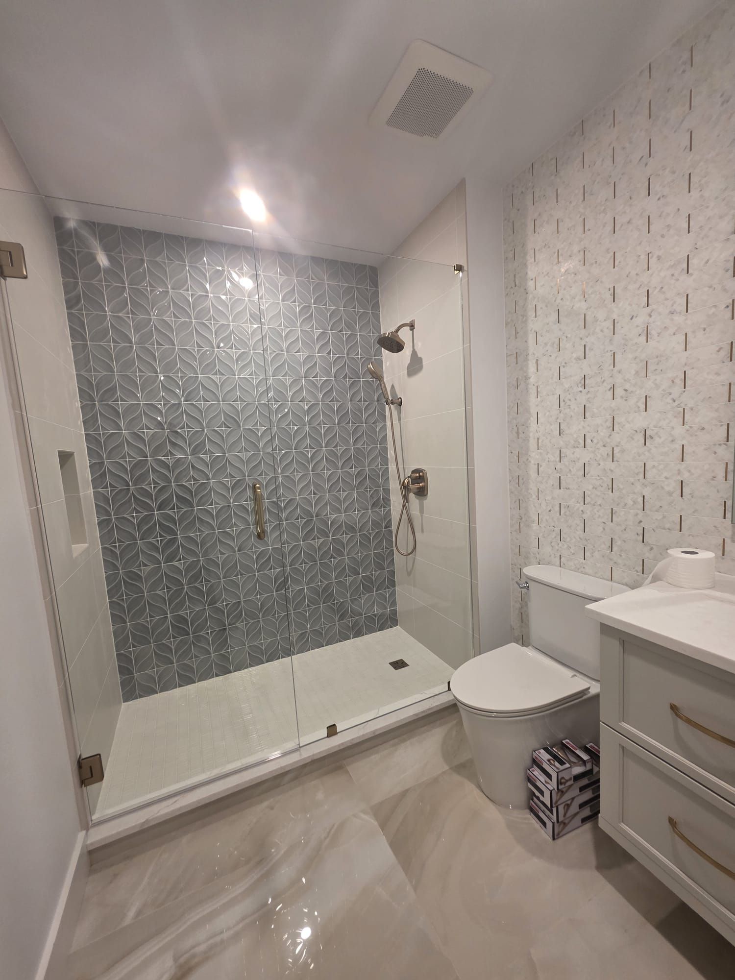 Modern bathroom with glass shower, patterned gray tile, and white walls and vanity.