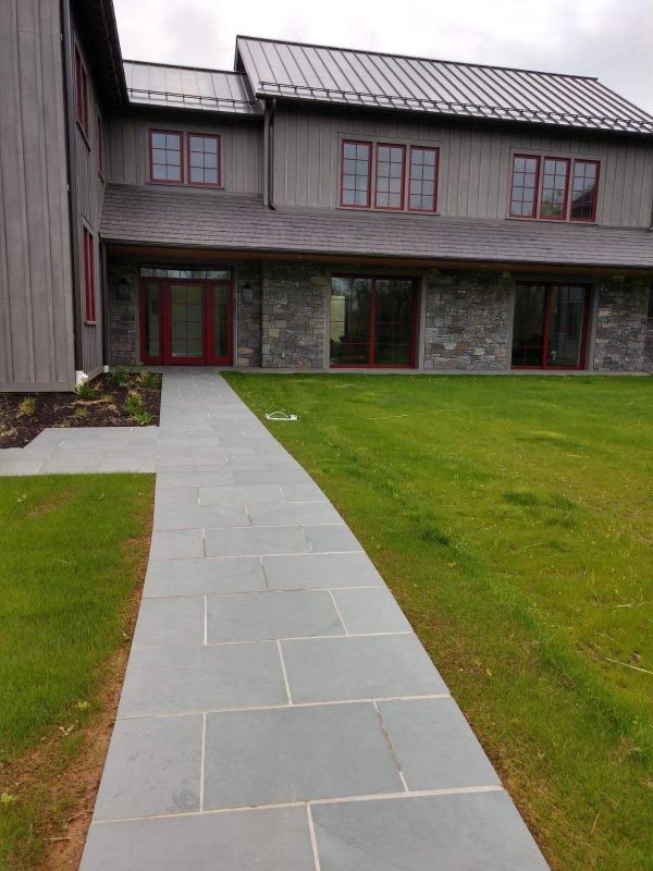 A stone walkway leading to a large house with a metal roof
