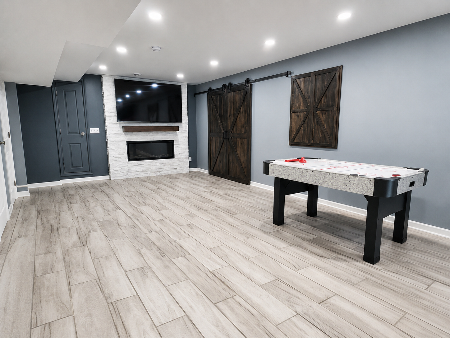 Modern basement rec room with gray walls, white wood floors, a TV, fireplace, and a black game table