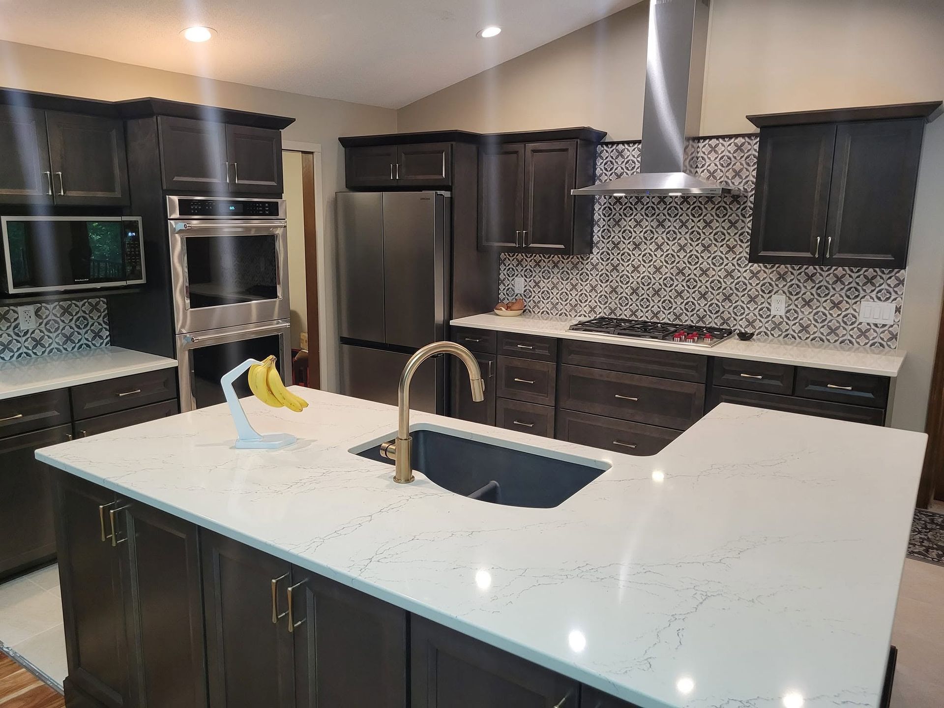 Modern kitchen with white island, dark cabinets, stainless appliances, and mosaic backsplash