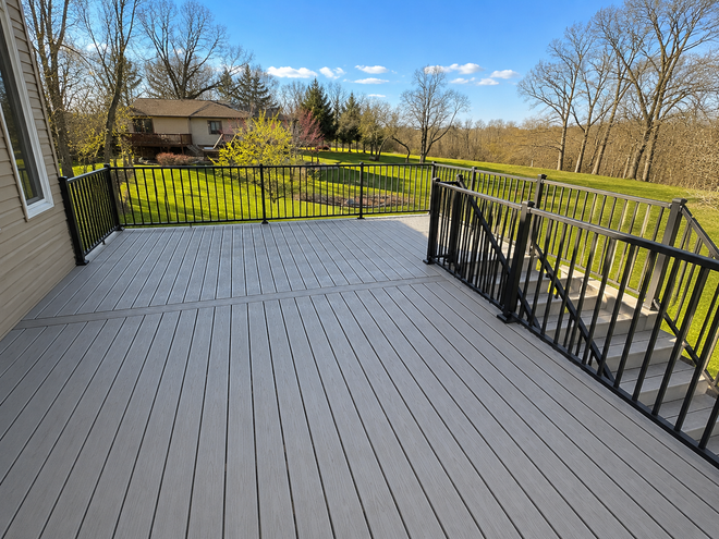 Spacious gray deck with black railings overlooking a sunny backyard and trees