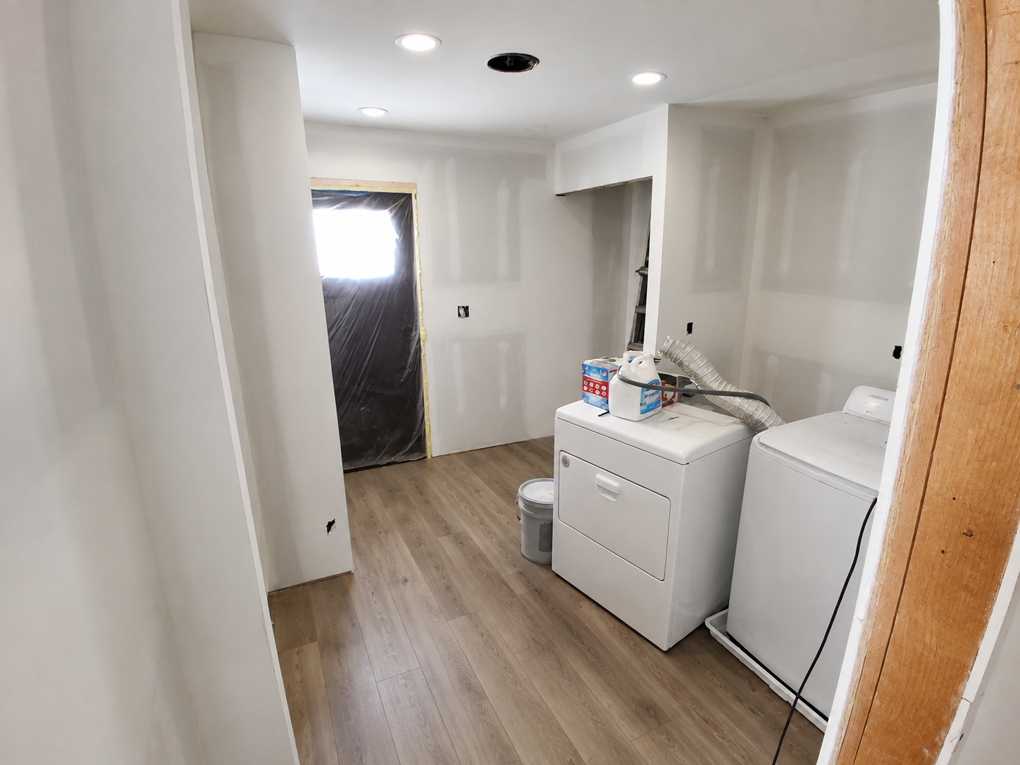Empty unfinished laundry room with white cabinets, washer, dryer, and a covered doorway near wood-look flooring.
