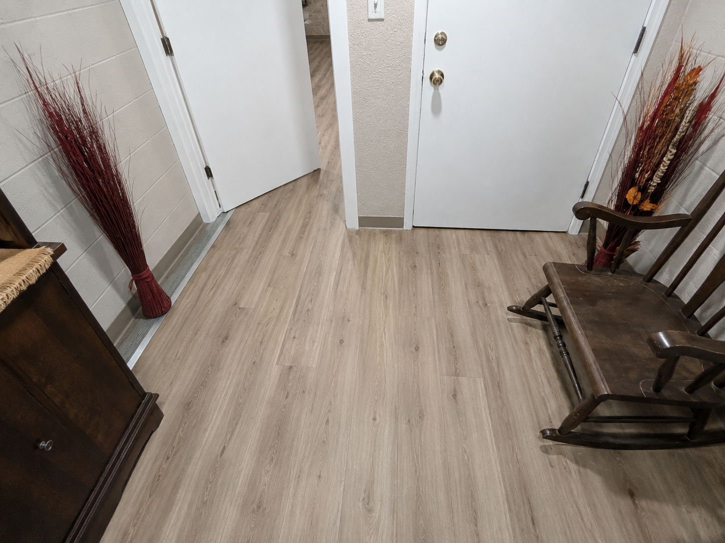 Hallway with white doors, light wood floor, decorative vases, and a wooden rocking chair