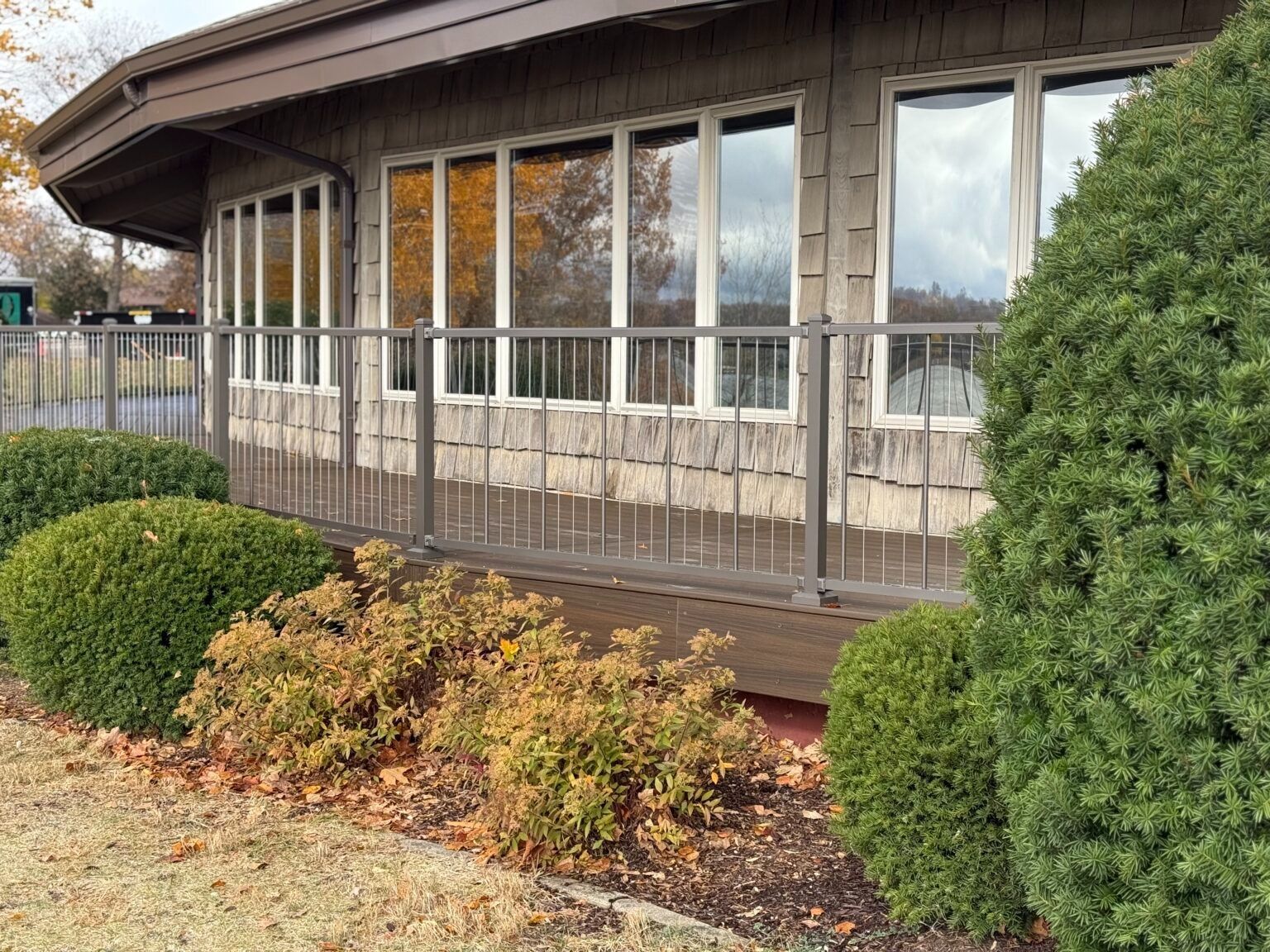 House exterior with large windows, wooden siding, and trimmed shrubs along the front garden.