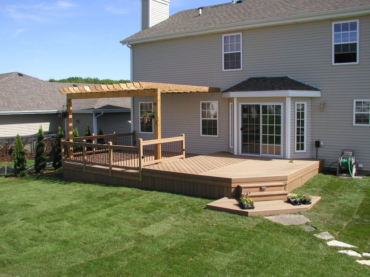 Backyard deck with pergola, wooden railings, and French doors beside a beige house