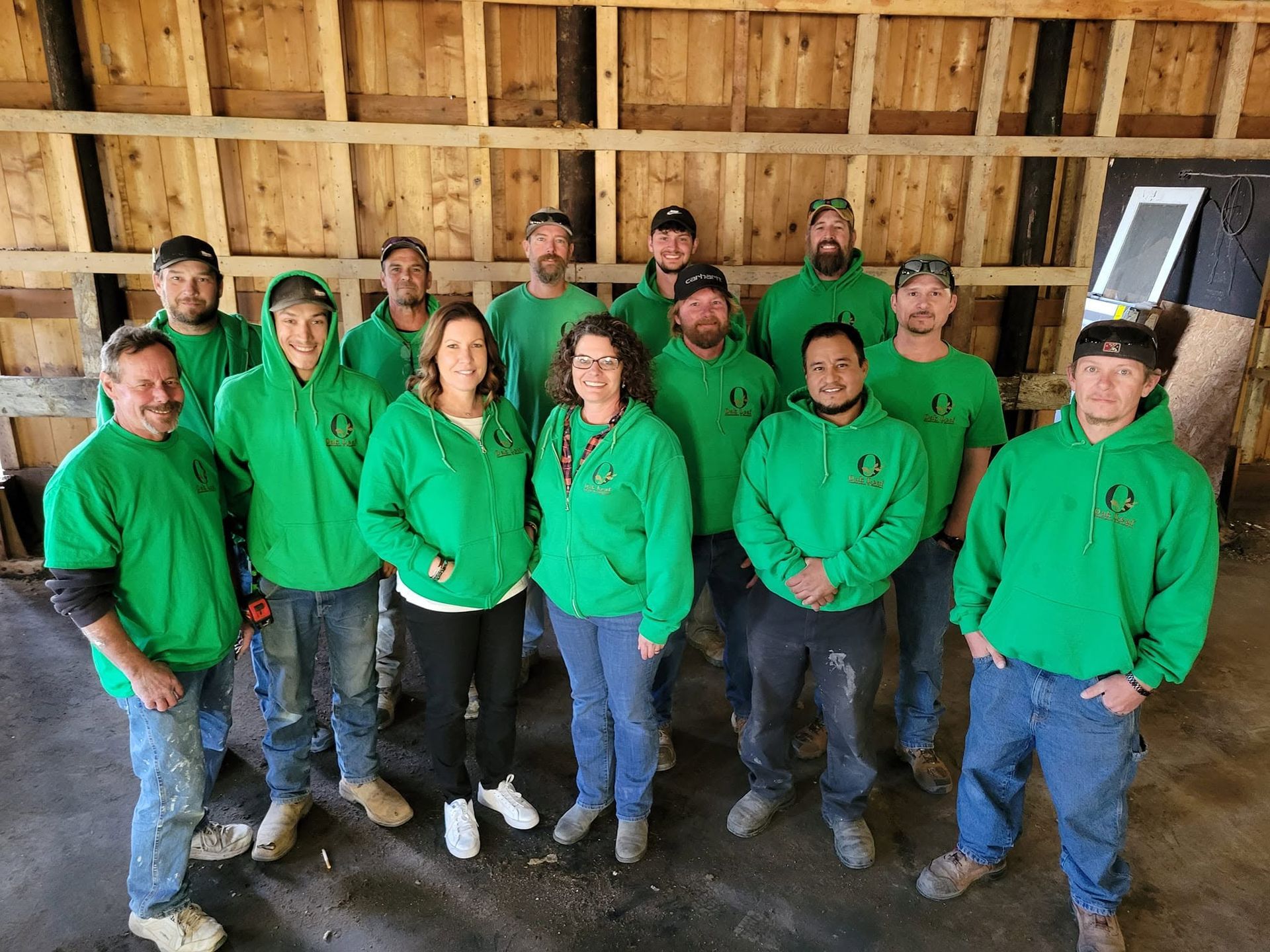 Group of people in green hoodies posing inside an unfinished wooden building frame