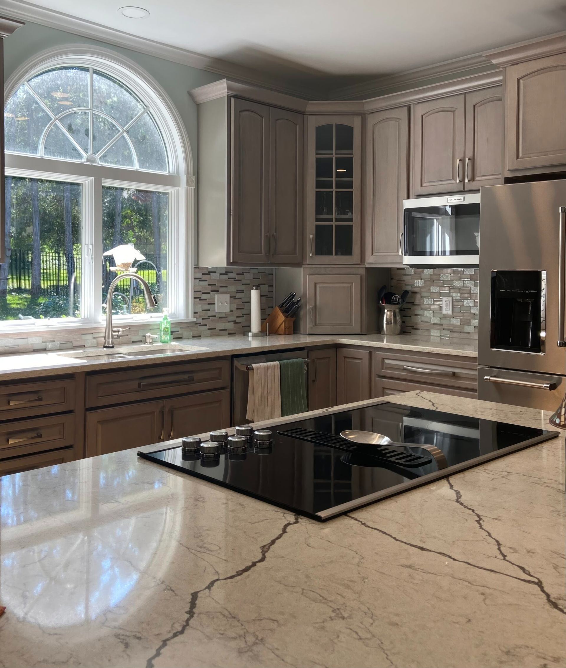 Bright modern kitchen with large arched window, beige cabinets, and a black island cooktop.