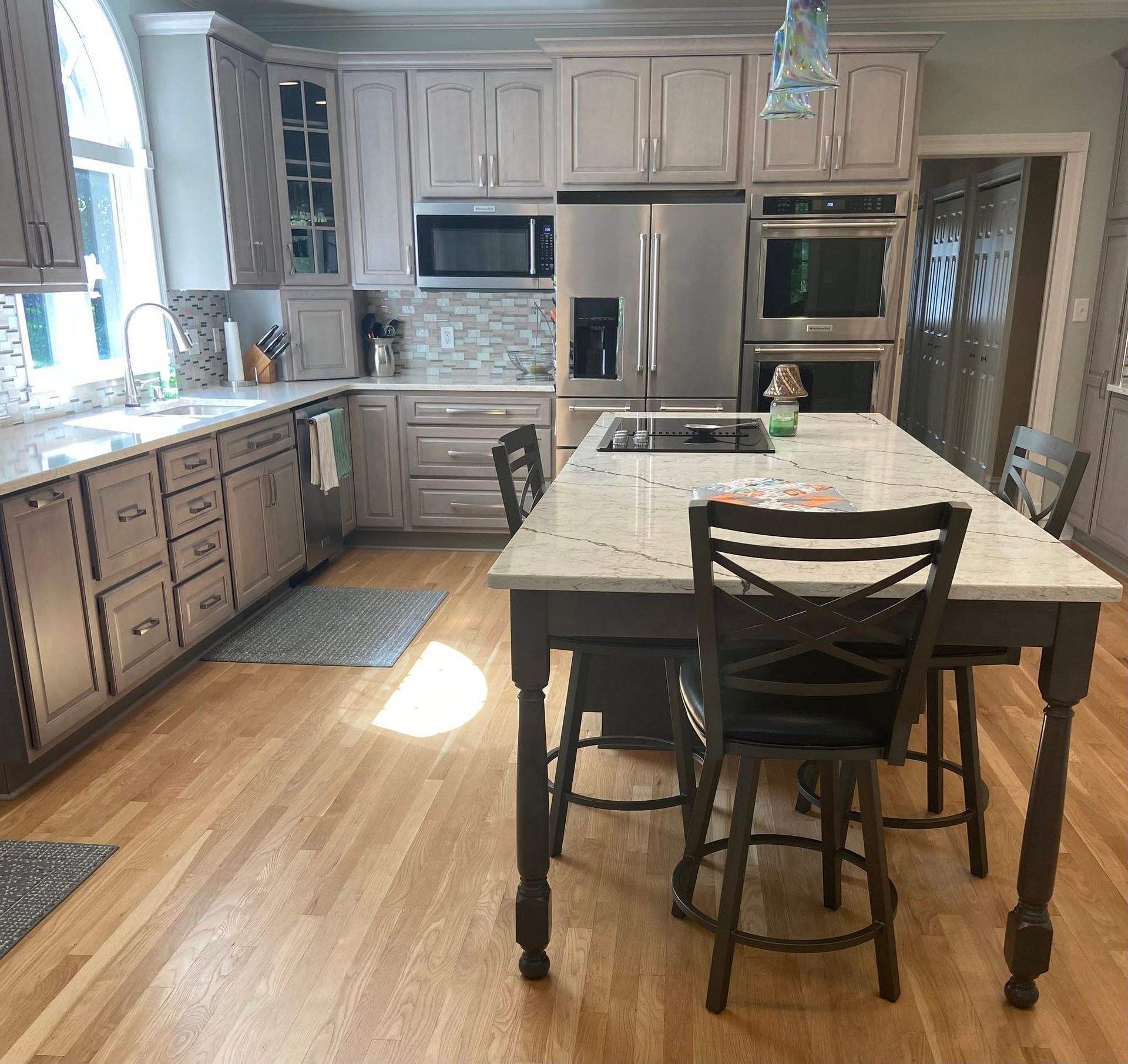 Bright kitchen with beige cabinets, granite island, stainless appliances, and a barstool on wood floors.