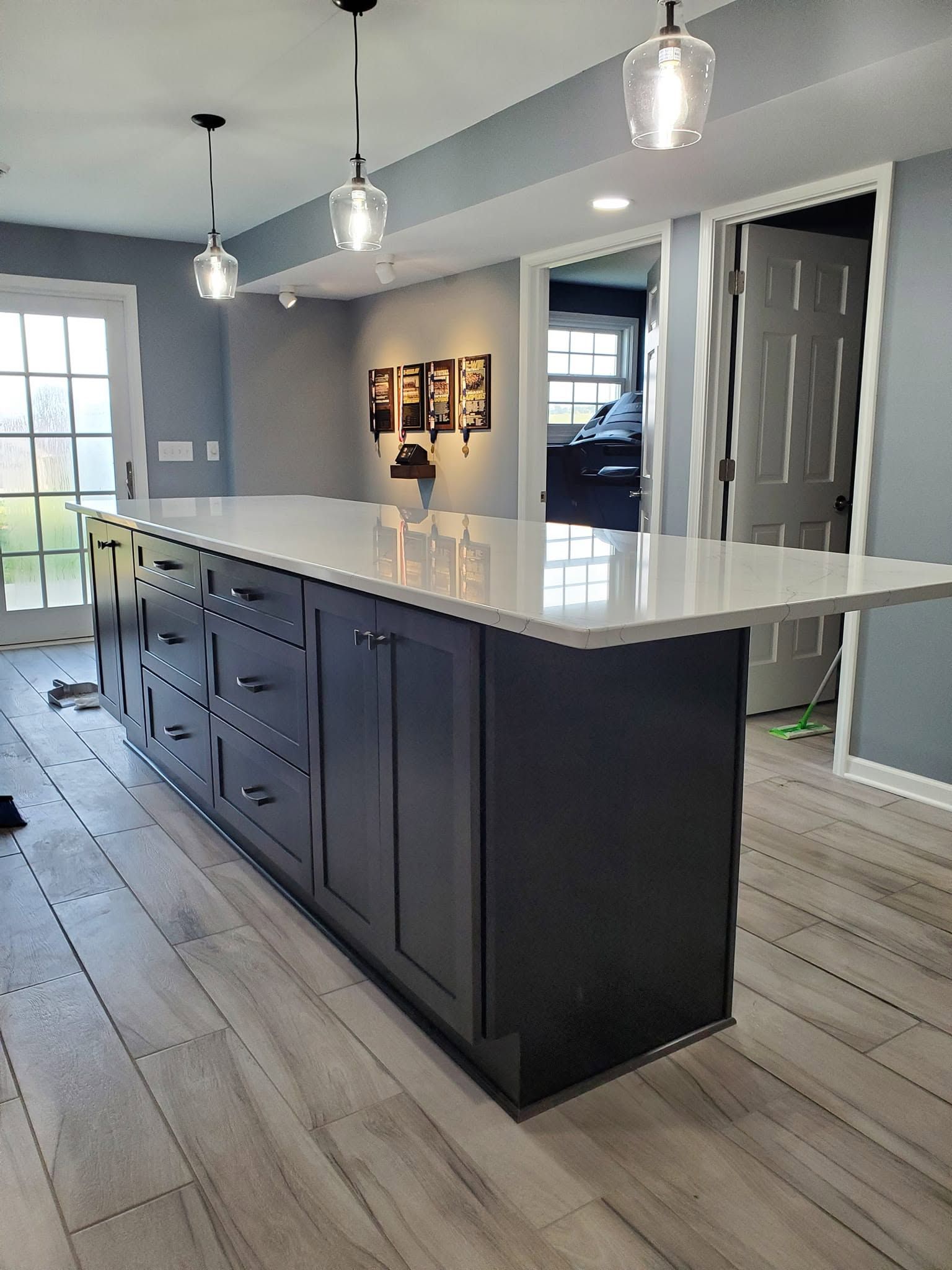 Modern kitchen with a large dark island, white countertops, pendant lights, and light wood flooring