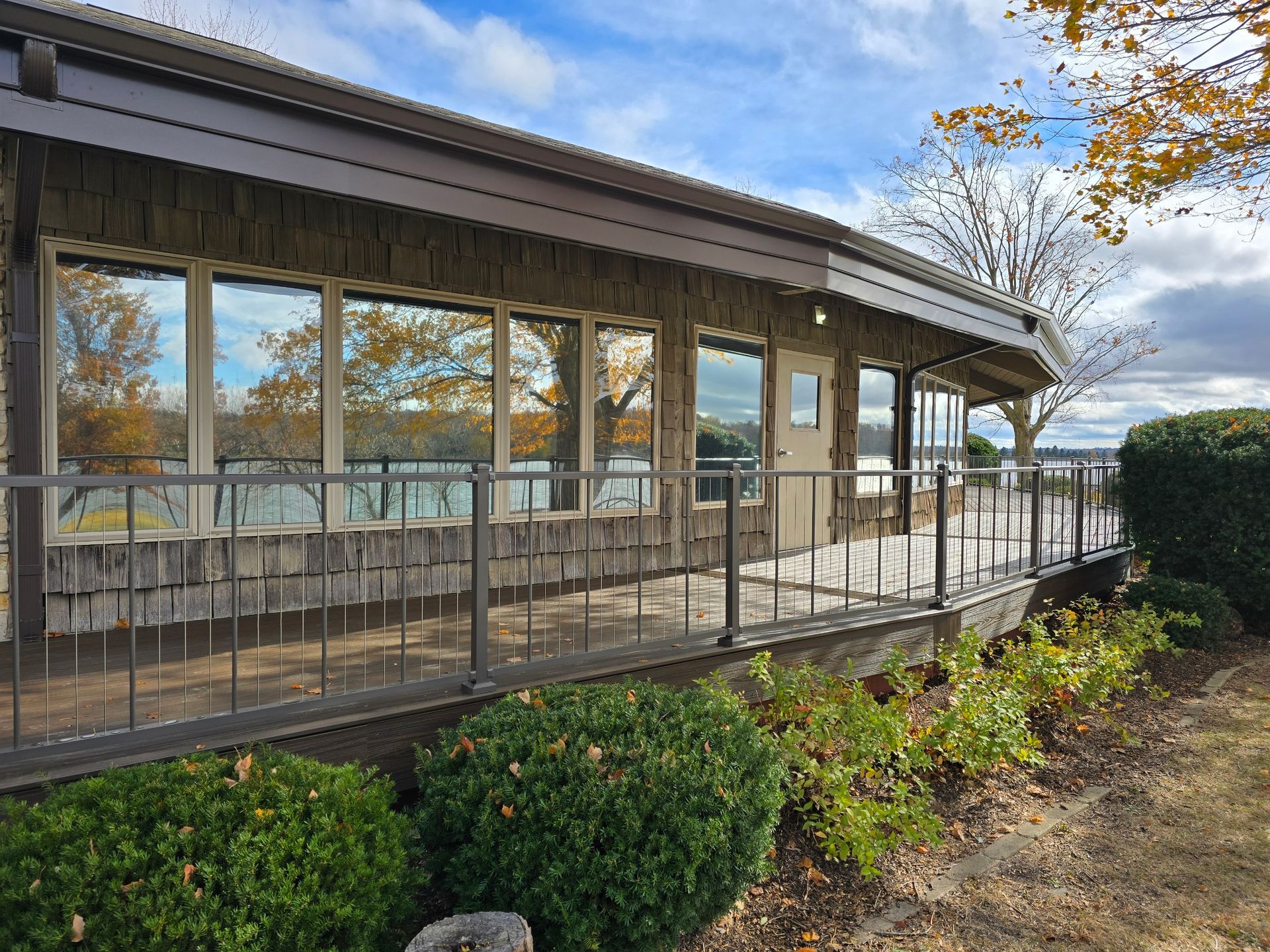 Wooden screened porch with large windows under a cloudy sky, surrounded by shrubs and trees