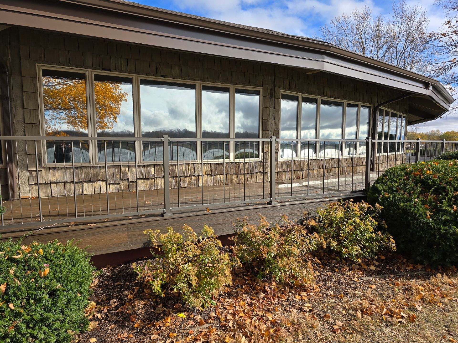 Curved glass building with a wooden deck and autumn shrubs in front